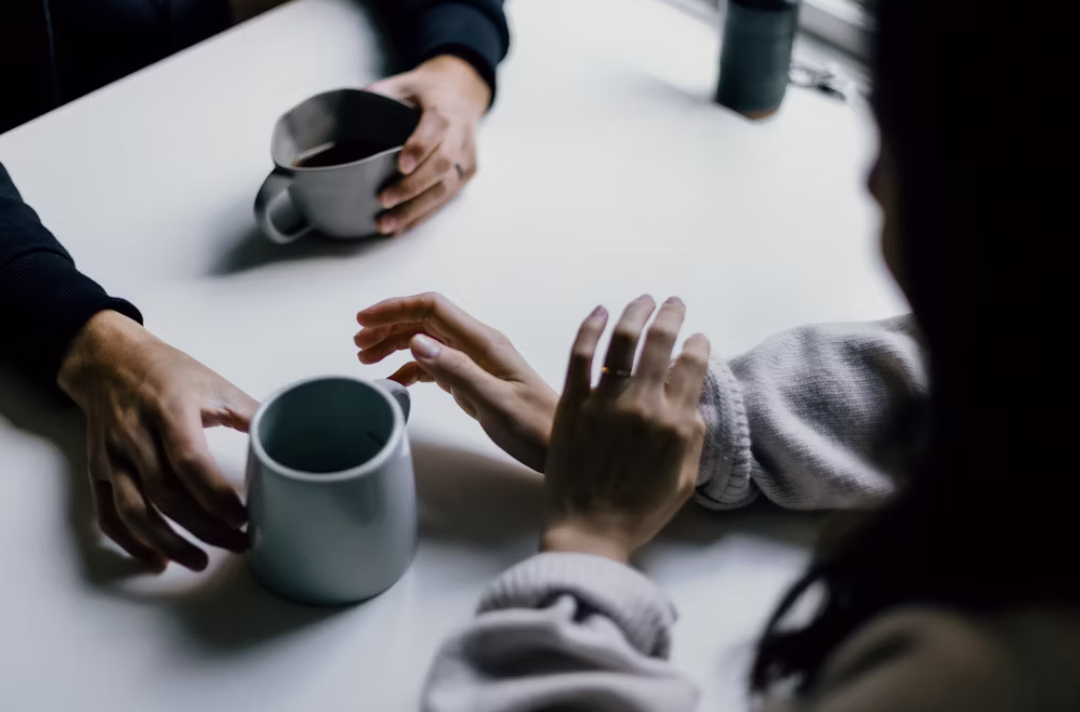 Neutral-toned photo showing two people's hands holding cups of black coffee during a meeting.