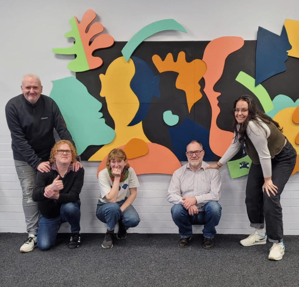 A photo of 5 people - part of the York MCN project - in the nursery room at York CVS with a collage in the background.