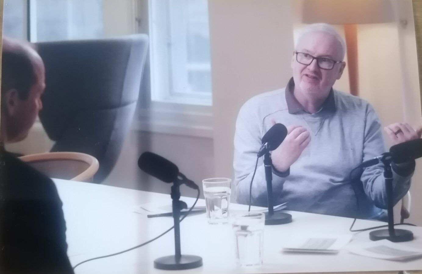 Miles is wearing a grey sweater, sitting behind a microphone facing Prince William as they record a podcast.