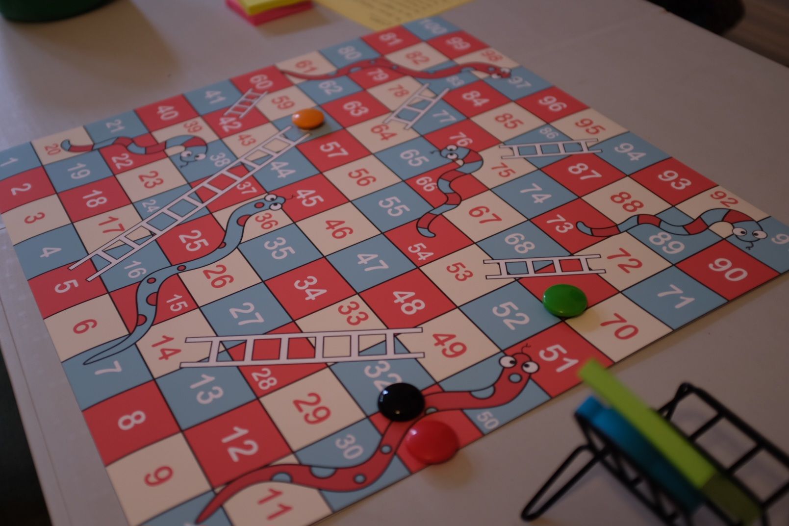 An image of a game of snakes and ladders on a table but the camera focusses in on a large green dice.